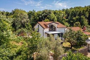 A modern two-story house with a tiled roof, surrounded by dense greenery.