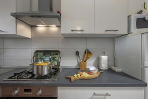 A modern kitchen with a gas stove, a pot on the stove, a wooden cutting board with food, and a white wall with cabinets. - Countryside Apartment Giani, Labin, Croatia (Labin)