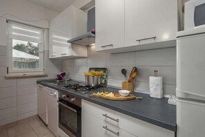 A modern kitchen with white cabinets, a gas stove, a dishwasher, and a window with a view. - Countryside Apartment Giani, Labin, Croatia (Labin)