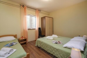 A room with two beds, a wardrobe, a window with curtains, a nightstand, and a lamp.