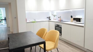 Una cocina moderna con armarios blancos, un microondas y un lavabo. Hay una mesa de comedor con dos sillas amarillas.