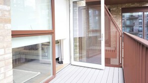 Un apartamento moderno con grandes puertas correderas de vidrio, una terraza de madera y vistas a edificios cercanos.