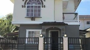 Una casa de dos pisos con entrada protegida por una reja, un balcón en el nivel superior y una ventana con barrotes.