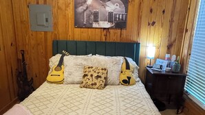 A wooden-paneled bedroom with a bed, pillows, and guitars. - Cozy cabin in pleasant Brewton with AC, WiFi, and fire pit.  (Brewton)