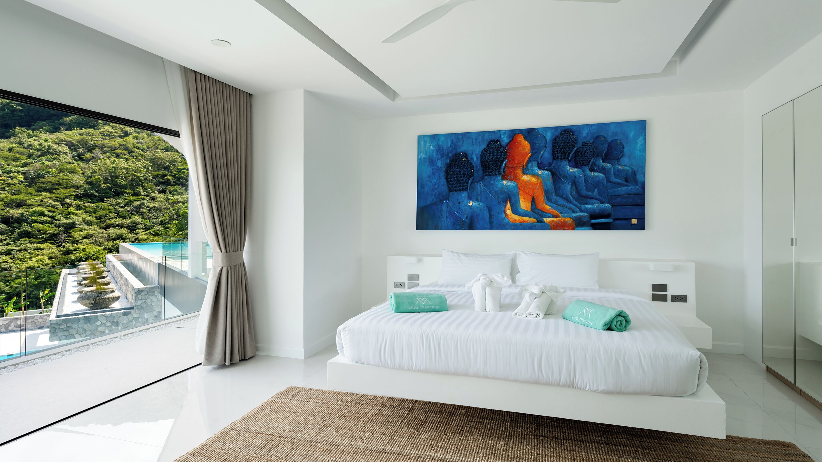 A modern bedroom with a large bed, a painting, and a view of a lush garden.
