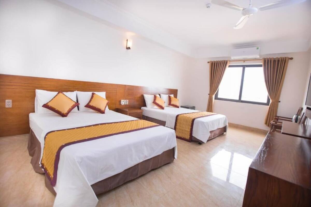 A hotel room with two beds, a wooden headboard, a desk, and a window with curtains.