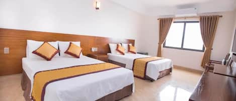 A hotel room with two beds, a wooden headboard, a desk, and a window with curtains.