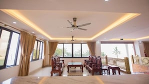 A spacious room with a large table and chairs, a ceiling fan, and large windows offering a view of the outdoors. - Tu Phuong Hotel TH by Bay Luxury (Hoang Thanh)