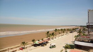 A beachside view with a clear sky, palm trees, and a building with a sign reading "Hung Thinh". - Tu Phuong Hotel TH by Bay Luxury (Hoang Thanh)