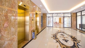 A lobby with marble walls, a patterned floor, and a glass door leading to a dining area. - Tu Phuong Hotel TH by Bay Luxury (Hoang Thanh)