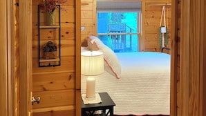 A cozy wooden room with a bed, a lamp, and a shelf with decorative items.