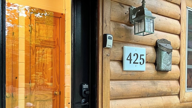 A wooden log cabin entrance with a black door, a mailbox, and a house number 425.