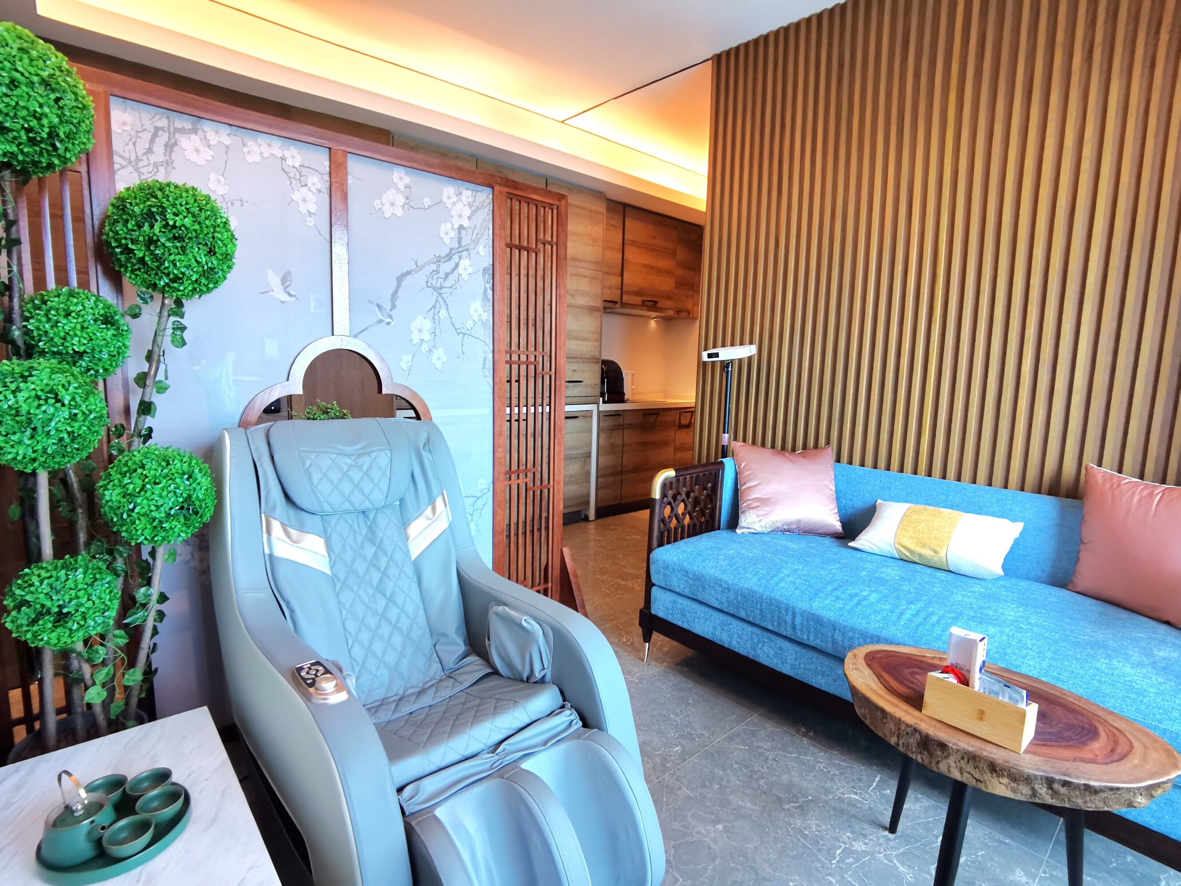 A modern room with a massage chair, a blue sofa, a small table with a tray, and a wall with vertical wooden slats.