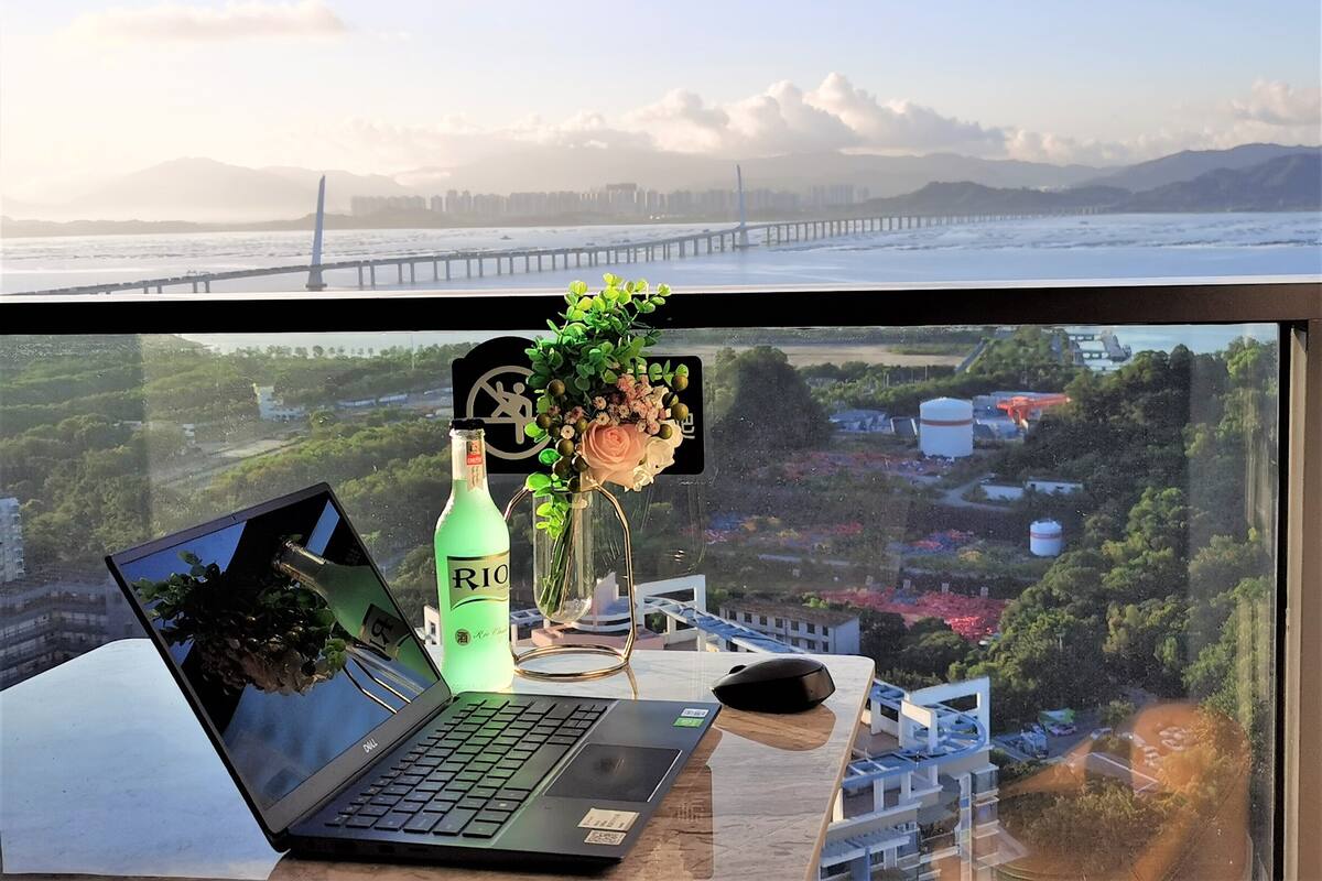 A laptop on a desk with a bottle of Rio beer, a vase with flowers, and a mouse.