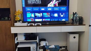 Una sala de estar moderna con televisor de pantalla plana mostrando la gira de un artista musical, una cafetera, un microondas y un altavoz.