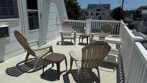 Un área de estar al aire libre con techo, sillones Adirondack y una mesa, rodeada por una barandilla blanca.