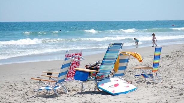 Una playa con varias sillas de descanso y una tabla de surf.