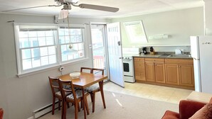 Cocina compacta con armarios de madera, un refrigerador blanco y un comedor con mesa y sillas.