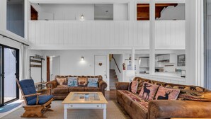 Un'ampia zona giorno con soffitto alto, un divano in pelle marrone con stampe animalier, una poltrona blu e un tavolino da caffè in legno.