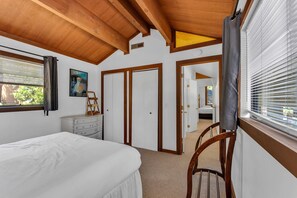 Quarto com cama, penteadeira, cadeira e porta que dá para outro cômodo.