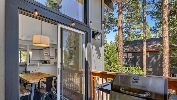 Una terrazza esterna moderna con barbecue, zona pranzo con tavolo e sedie, e una porta scorrevole in vetro che dà su una cucina.