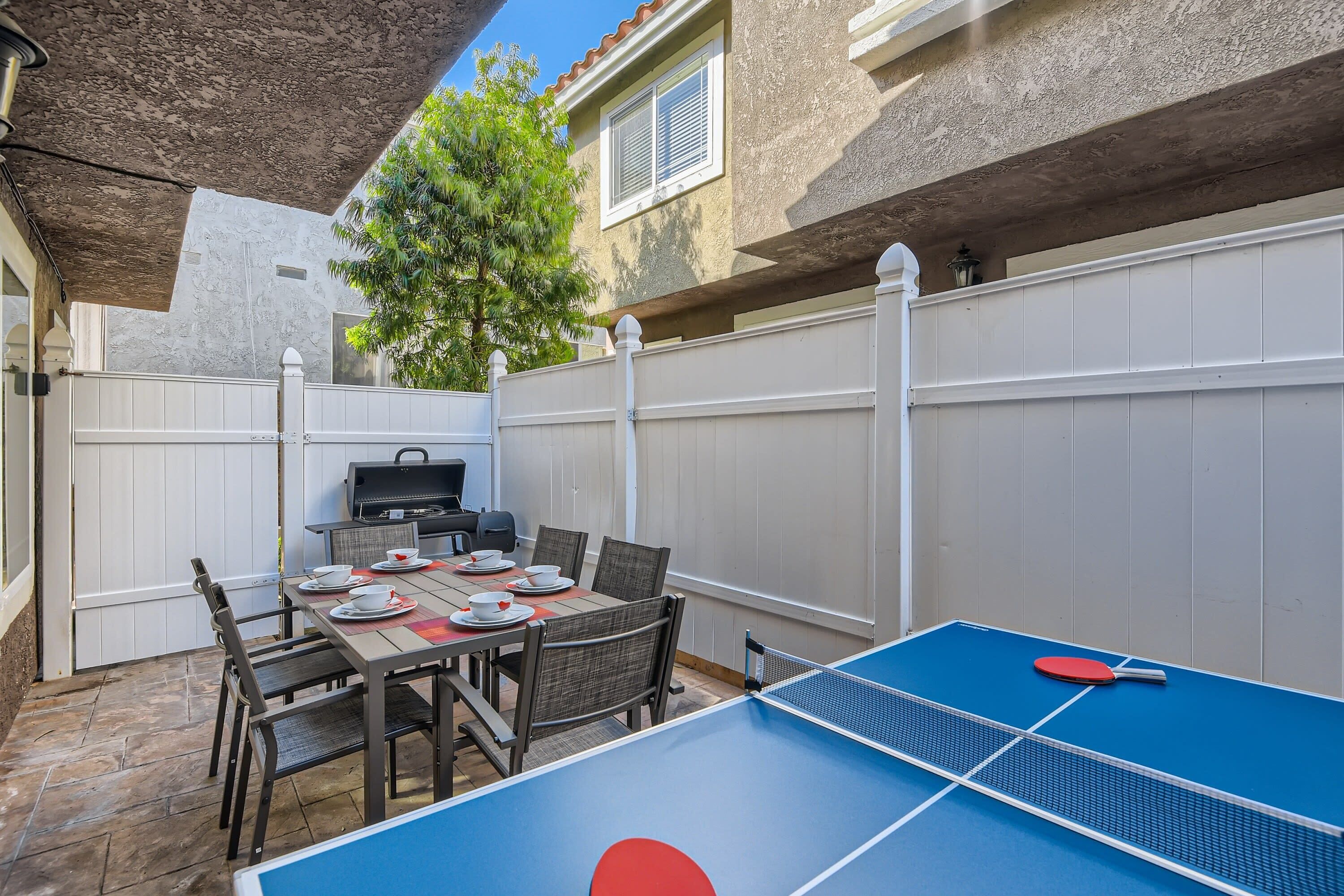 Une terrasse extérieure équipée d’une table de ping-pong, d’une table à manger avec des chaises et d’un barbecue.