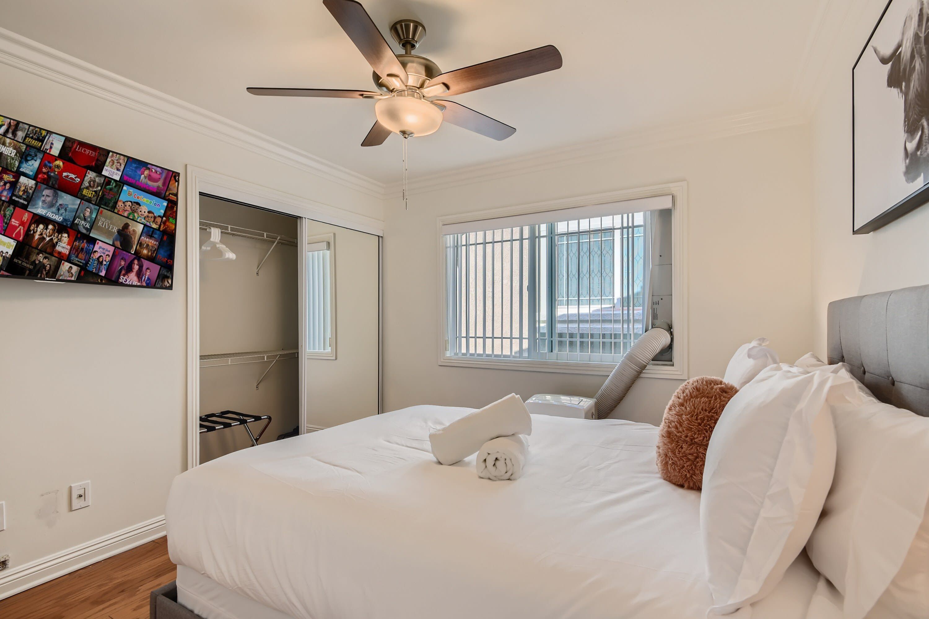 Ein Hotelzimmer mit einem Bett, einem Deckenventilator, einem Fenster mit Jalousien, einer Wandcollage mit Fotos und einer Tür zu einem Badezimmer.