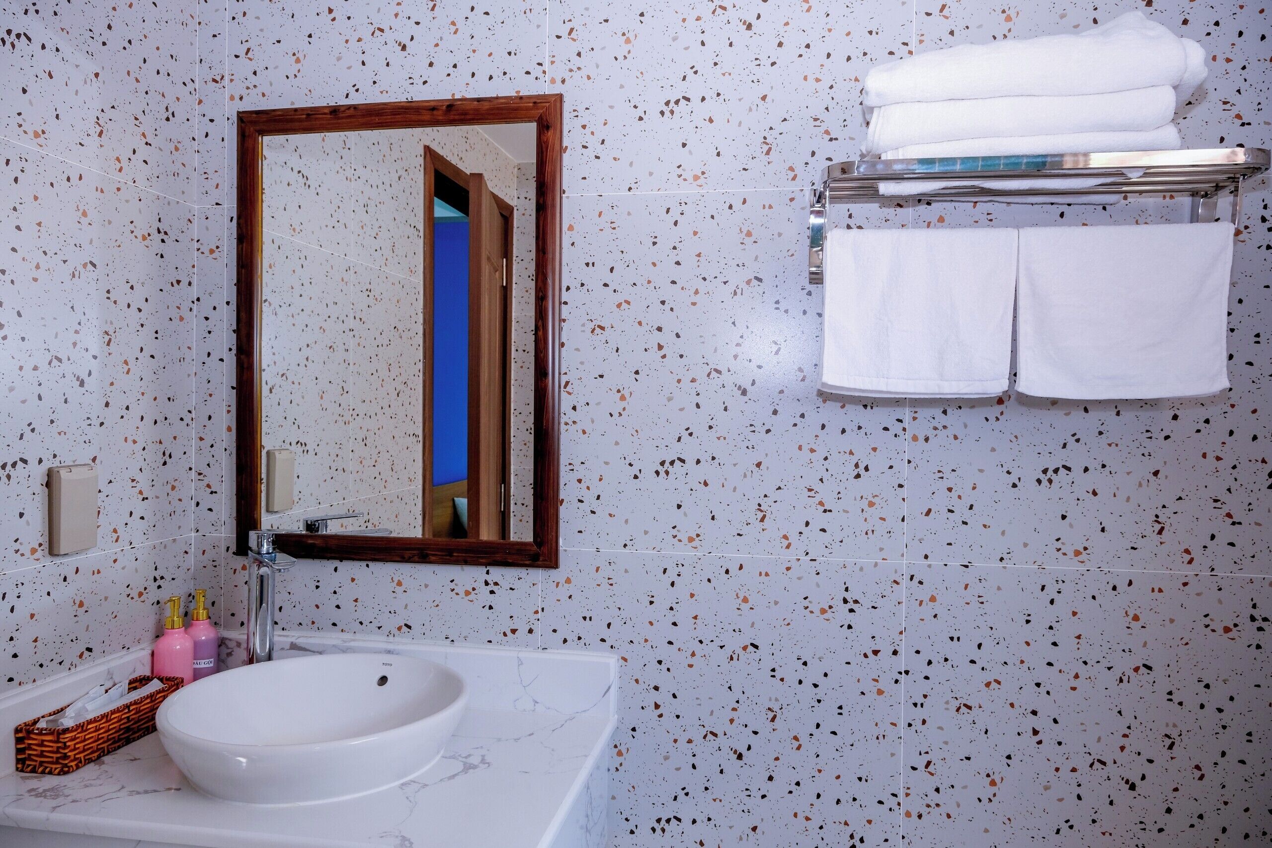 Un baño con un lavamanos blanco, un espejo con marco de madera y un perchero con toallas dobladas.
