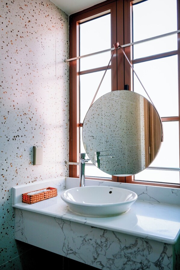 A bathroom with a white marble sink, a round mirror, and a window with wooden frames.