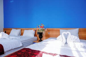 Habitación de hotel con dos camas, cabecero de madera, un florero con flores y toallas dispuestas en forma de corazón.