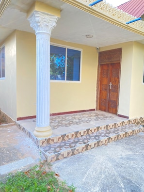 A building entrance with a large white column, a wooden door, and a window. - Spacious 2-Bedroom Apartment in Zanzibar with Free Parking & Entertainment (Zanzibar)