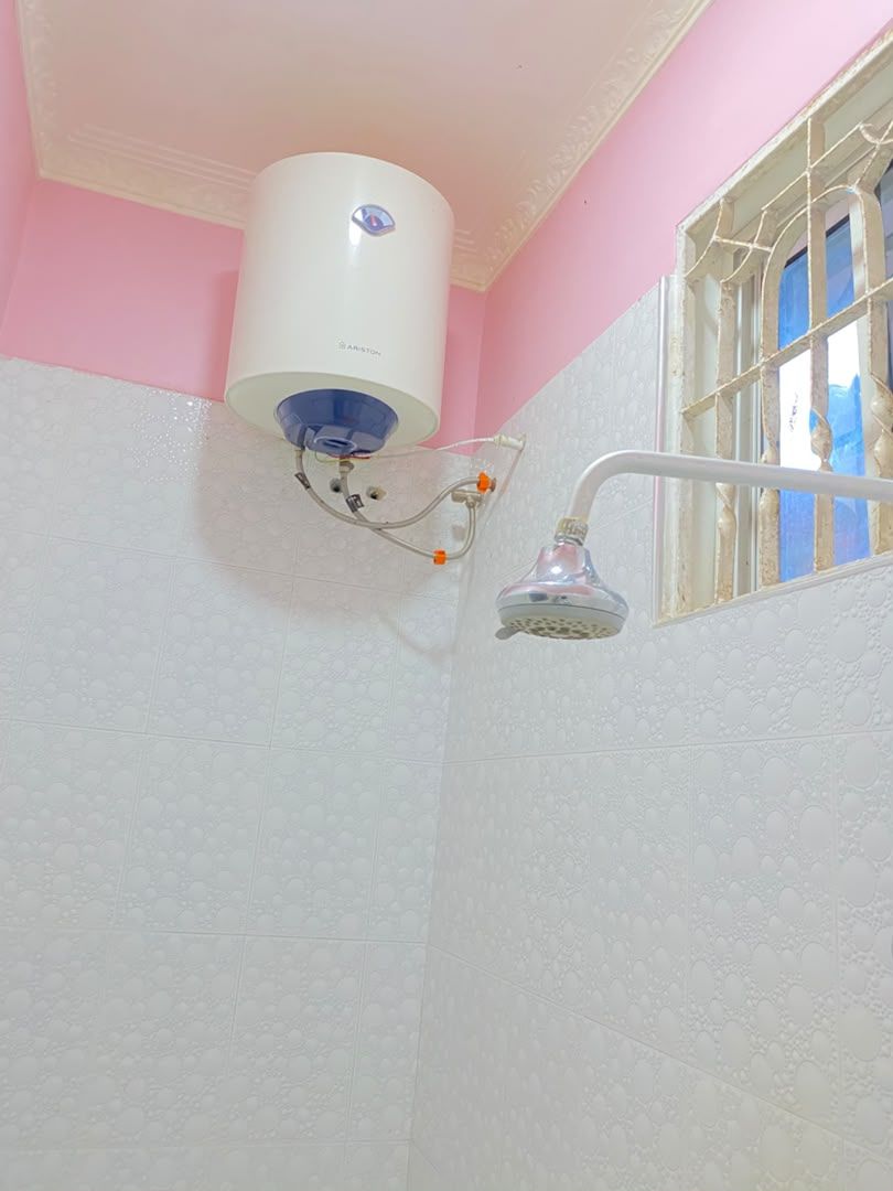 Une salle de bain avec une douche, un mur blanc et une fenêtre avec des barreaux.
