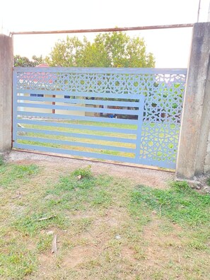 A blue metal gate with a lattice design, standing in a grassy area with concrete pillars.