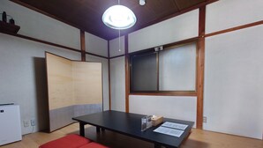 Una habitación con suelo de madera, una mesa negra con cojín rojo, un aire acondicionado blanco y una lámpara en el techo.