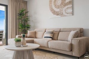A beige sofa with two cushions, a round table with decorative items, and a large abstract painting on the wall. - Breeze | pool - views - gym (La Cala de Mijas)