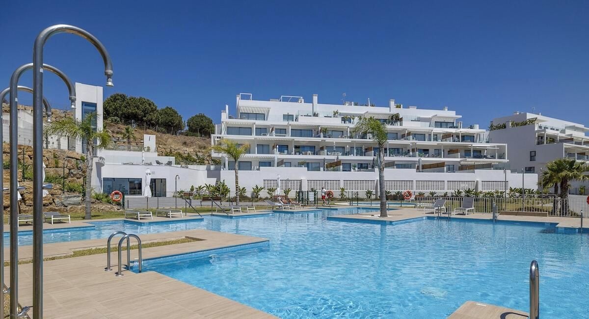 Una piscina con varios niveles de balcones, rodeada por un área ajardinada con palmeras.