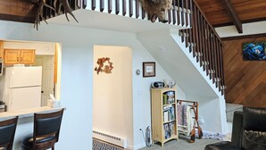 Amplia sala de estar con techo alto, una escalera de madera y una cabeza de animal montada.