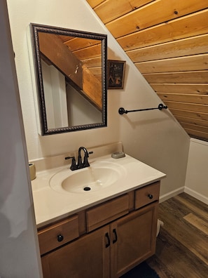 A bathroom with a white sink, wooden vanity, and a mirror with a decorative frame.
