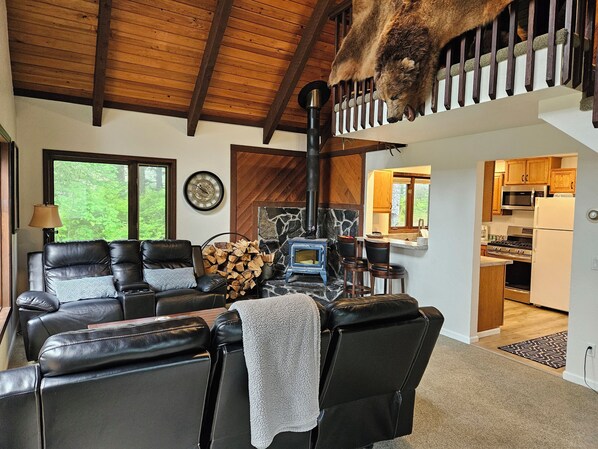 A cozy living room with a fireplace, leather sofa, and a dining area with wooden cabinets.
