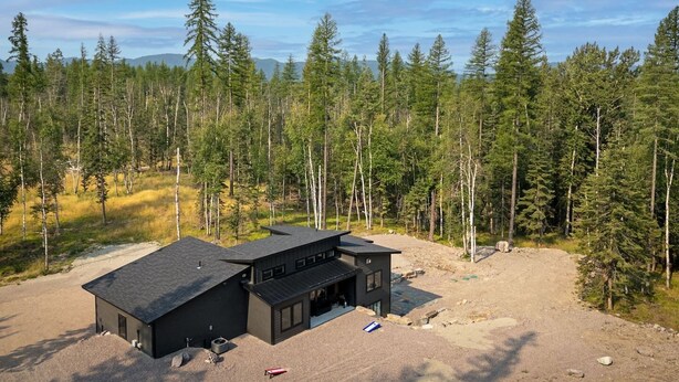 Un bâtiment moderne à deux étages, doté d’une façade sombre, entouré d’une zone boisée.