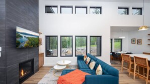 Un salon moderne avec une cheminée, un canapé bleu et un coin repas avec des chaises en bois.