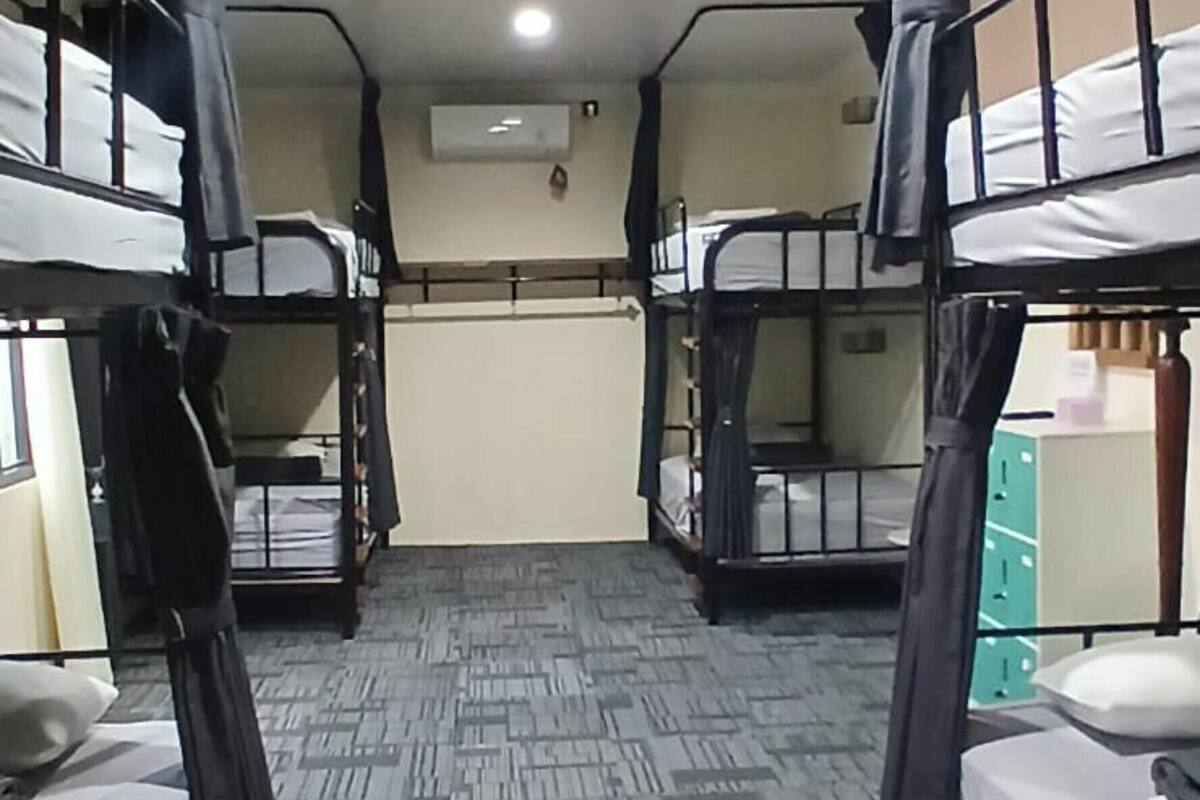 A dormitory room with bunk beds, a carpeted floor, and an air conditioning unit on the wall.
