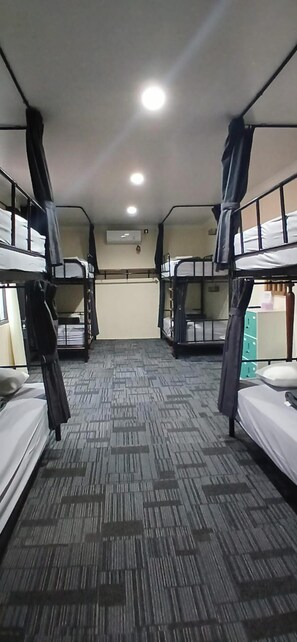 A dormitory room with bunk beds, a carpeted floor, and an air conditioning unit on the wall. - Musafir Guest House Syariah (Surakarta)