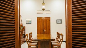 A dining area with a wooden table and chairs, a wooden door, and a hanging light fixture. - Musafir Guest House Syariah (Surakarta)