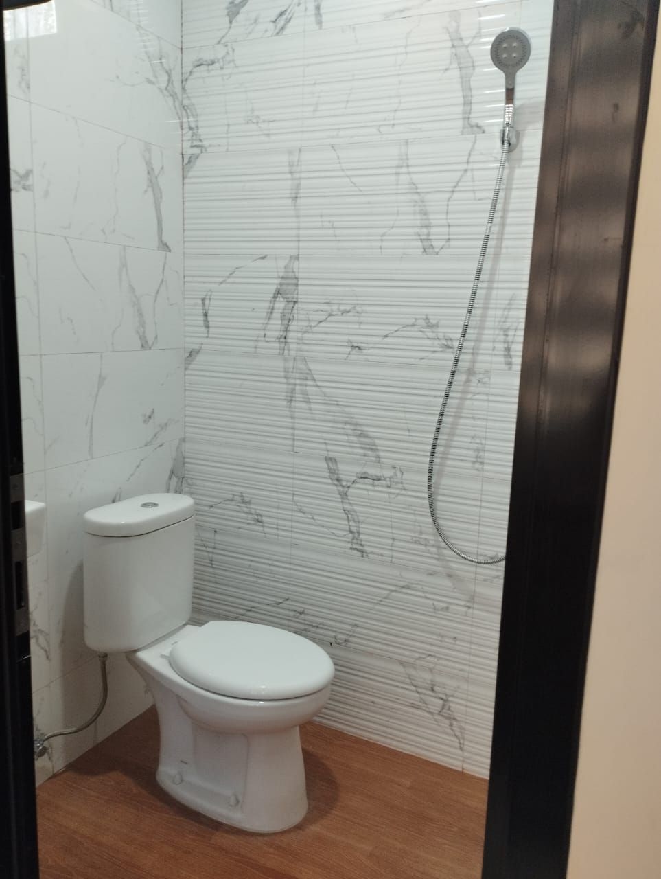 Un baño con inodoro, ducha y paredes con diseño de mármol.