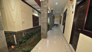 A hallway with a tiled floor, a small garden area with plants, and a door on the right. - Musafir Guest House Syariah (Surakarta)