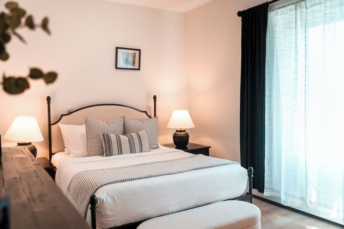 A neatly made bed with pillows, a bedside lamp, and a window with curtains.