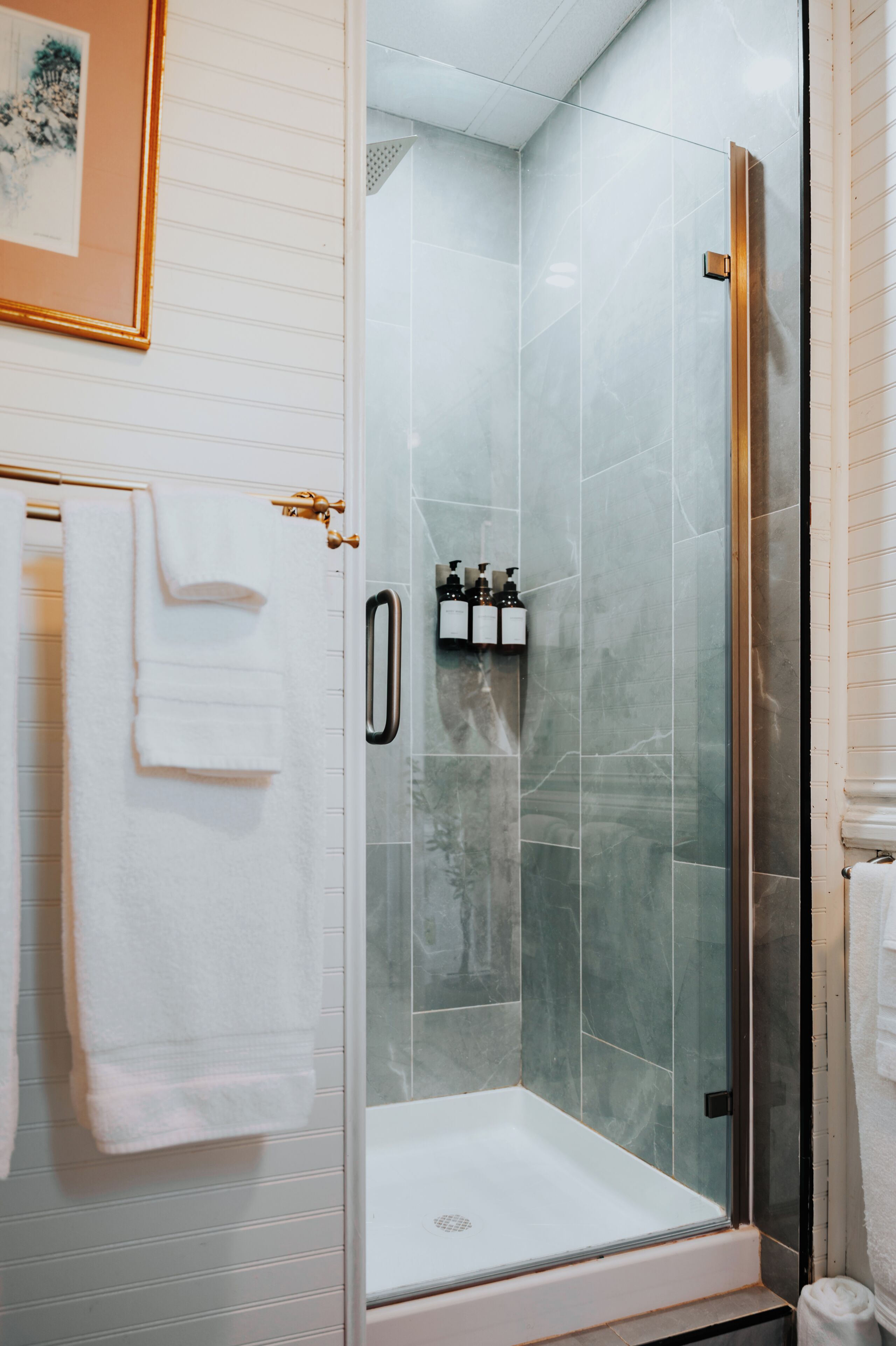 Un box de ducha con paredes de azulejos blancos y un cuadro enmarcado sobre él.