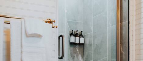 A glass-enclosed shower stall with a white tiled wall and a framed picture above it.
