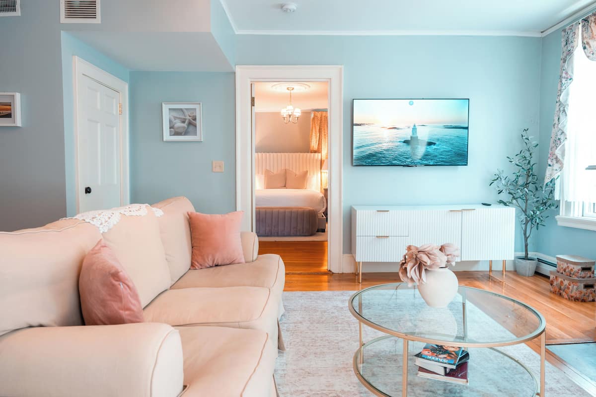 A living room with a sofa, a glass coffee table, a TV, and a door leading to a bedroom.